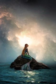 a mermaid sitting on top of a rock in the ocean