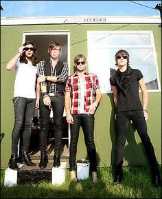 three young men standing in front of a small green building with their hands on their hipss