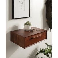 a wooden shelf with a plant on it next to a white wall and framed artwork