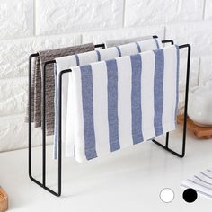 three towels are hanging on a rack in front of a white brick wall and wooden cutting board