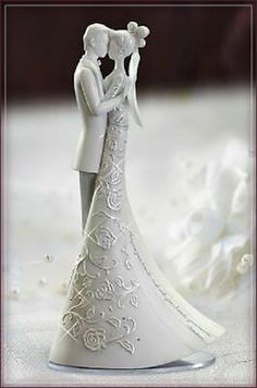 a bride and groom figurine standing next to each other on a white surface