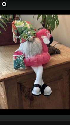 a small doll sitting on top of a wooden table next to a potted plant