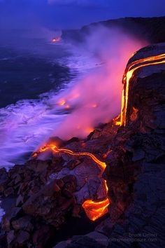 an ocean cliff with lava flowing out of it and glowing lights on the rocks below