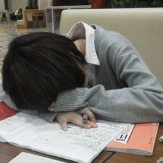 a person sitting at a table with their head in his hands and writing on paper