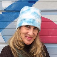 a woman wearing a tie dye hat standing in front of a painted wall and smiling at the camera