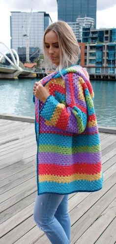 a woman is standing on a dock wearing a colorful crochet sweater and jeans