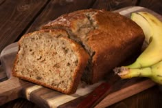 a loaf of banana bread sitting on top of a cutting board next to two bananas