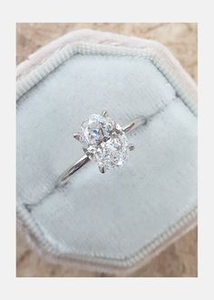 an oval diamond ring sitting on top of a cushion