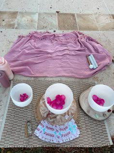 three bowls with flowers in them sitting on a mat next to a towel and two cups