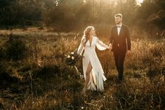 a bride and groom holding hands walking through tall grass with the sun shining on them