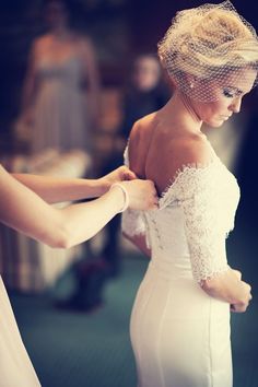 a woman in a white wedding dress adjusting the veil on another woman's shoulder