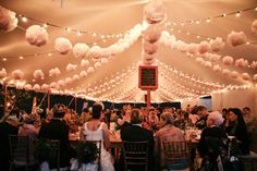 an event tent with many people sitting at tables and balloons hanging from the ceiling above it