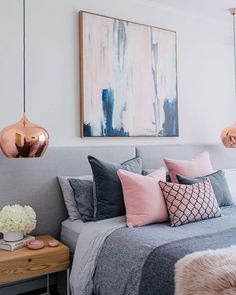 a bedroom with pink and grey decor on the walls, gray bedding, white pillows, and gold accents