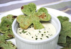 a white plate topped with chips and a shamrock shaped dip in a bowl surrounded by green leaves