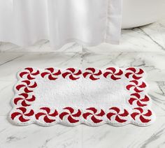 a bathroom rug with red and white designs on the floor next to a bath tub