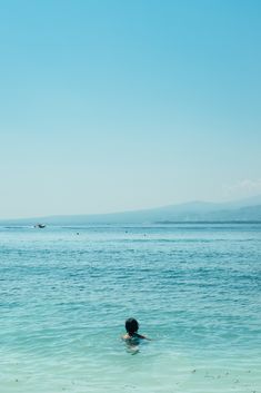 a person swimming in the ocean on a clear day with mountains in the back ground