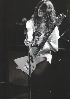 a black and white photo of a man with long hair holding a guitar in front of a microphone