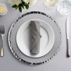 a place setting with napkins and silverware on a gray table cloth, white flowers in the background