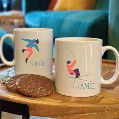 two white coffee mugs sitting on top of a wooden table next to a cookie