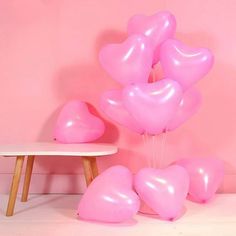 a bunch of pink heart shaped balloons in front of a white table and chair against a pink wall