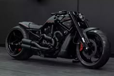 a black and red motorcycle parked in front of a gray wall on concrete flooring