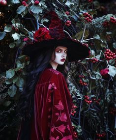 a woman with long hair wearing a red dress and black hat standing in front of flowers