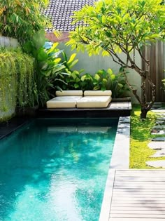 an outdoor swimming pool surrounded by greenery and wooden decking, with lounge chairs on the side