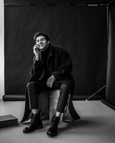 a black and white photo of a man sitting on a stool talking on his cell phone