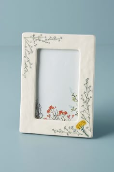 a white photo frame with flowers painted on the front and bottom, sitting on a blue surface