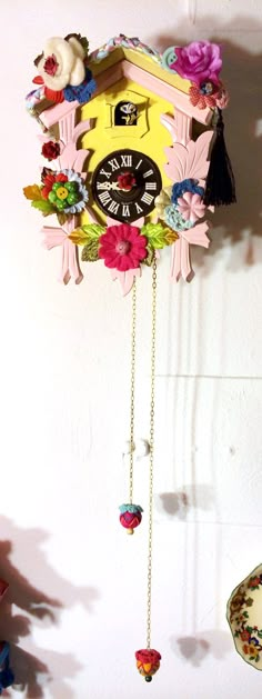 a colorful clock hanging from the side of a wall next to a vase with flowers on it