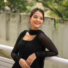 a woman standing next to a white fence wearing a black dress and smiling at the camera