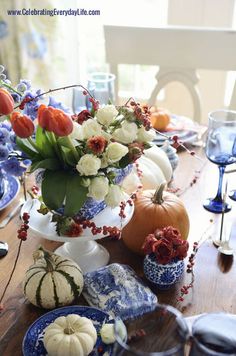 a table topped with blue and white dishes filled with flowers, pumpkins and other decorations