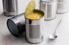 an open tin can with a pickle in it next to other cans and spoons