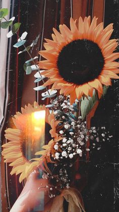 a woman's hand holding a vase with sunflowers and a candle in it