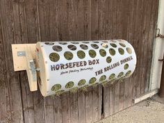 a horse feed box mounted to the side of a wooden fence with grass growing in it