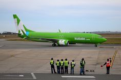 a group of people standing on the tarmac next to an airplane that is green and white