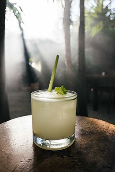 a drink sitting on top of a wooden table next to some trees in the background