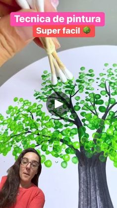 a woman is painting a tree with green leaves