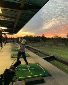 a man swinging a golf club on top of a green course at sunset with the sun setting in the background