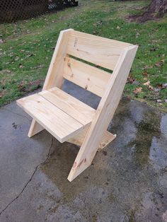 a wooden chair sitting on top of a cement ground next to a grass covered field