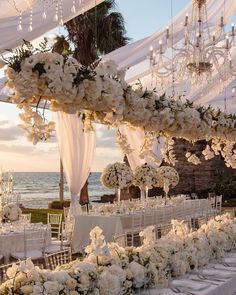 an outdoor wedding setup with white flowers and chandeliers at the head table, overlooking the ocean