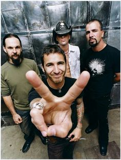 a group of men standing next to each other in front of a metal wall holding their hands up