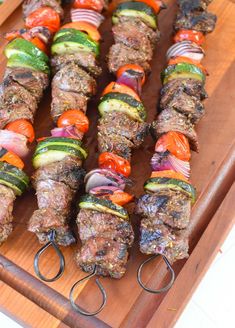 several skewers of meat and vegetables on a wooden tray