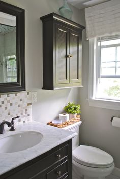 a white toilet sitting next to a sink in a bathroom under a window with blinds