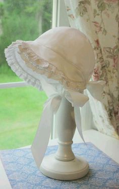 a white bonnet sitting on top of a table in front of a window sill