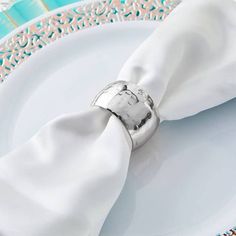 a white plate topped with a napkin and silver ring on it's center piece