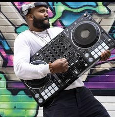 a man holding a dj controller in front of a graffiti wall