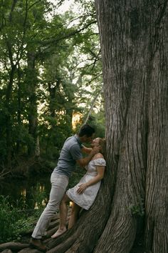 a man and woman kissing in front of a large tree with its roots growing into the ground