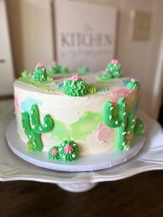 a white cake with green frosting and cactus decorations on it sitting on a plate