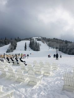 many white chairs are set up in the snow for a ski slope wedding ceremony on a cloudy day